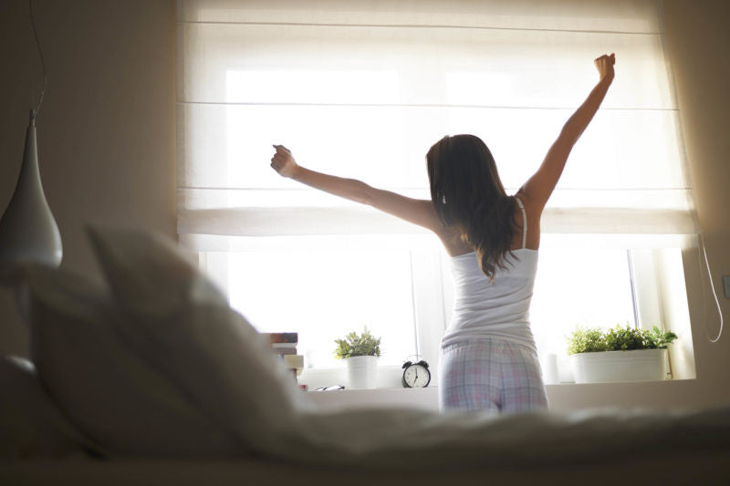 sleepy woman stretching in front of her window