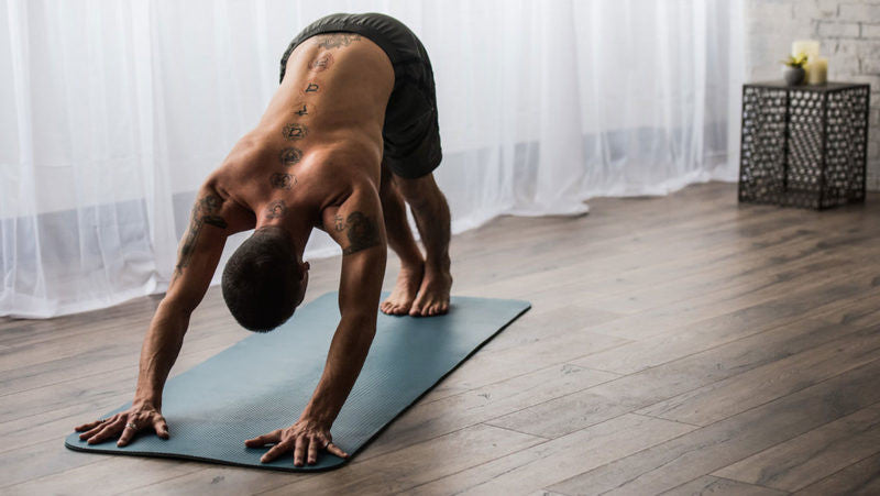 shirtless man does down dog on yoga mat